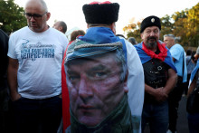 Muž s vlajkou vo farb&aacute;ch srbskej vlajky a s fotografiou b&yacute;val&eacute;ho bosniansko-srbsk&eacute;ho vojnov&eacute;ho gener&aacute;la Ratka Mladića stoj&iacute; medzi ľuďmi zhromažden&yacute;mi v Kostole sv. Luk&aacute;&scaron;a. FOTO: Reuters