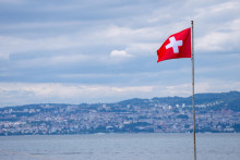 FILE PHOTO: A Swiss flag is pictured in front of the Swiss city of Lausanne ahead of a June 14 vote on a proposal from the right-wing Swiss People&lsquo;s Party to cap the population at 10 million inhabitants by 2050, in Evian-les-Bains, France, June 12, 2026. REUTERS/Denis Baliboouse/File Photo FOTO: Denis Balibouse