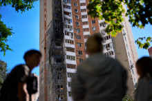 Miestni obyvatelia sa pozeraj&uacute;, ako hasiči hasia požiar čiastočne zničenej obytnej budovy po ruskom dronovom &uacute;toku v Kyjeve v stredu 9. septembra 2026. FOTO: TASR/AP