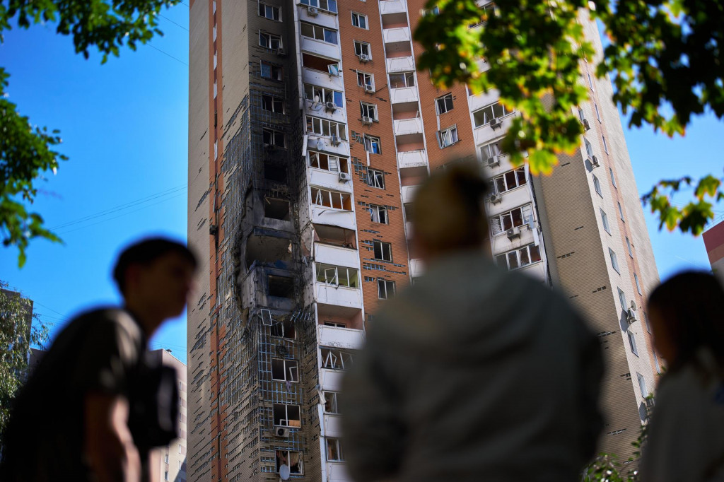 Miestni obyvatelia sa pozeraj&uacute;, ako hasiči hasia požiar čiastočne zničenej obytnej budovy po ruskom dronovom &uacute;toku v Kyjeve v stredu 9. septembra 2026. FOTO: TASR/AP